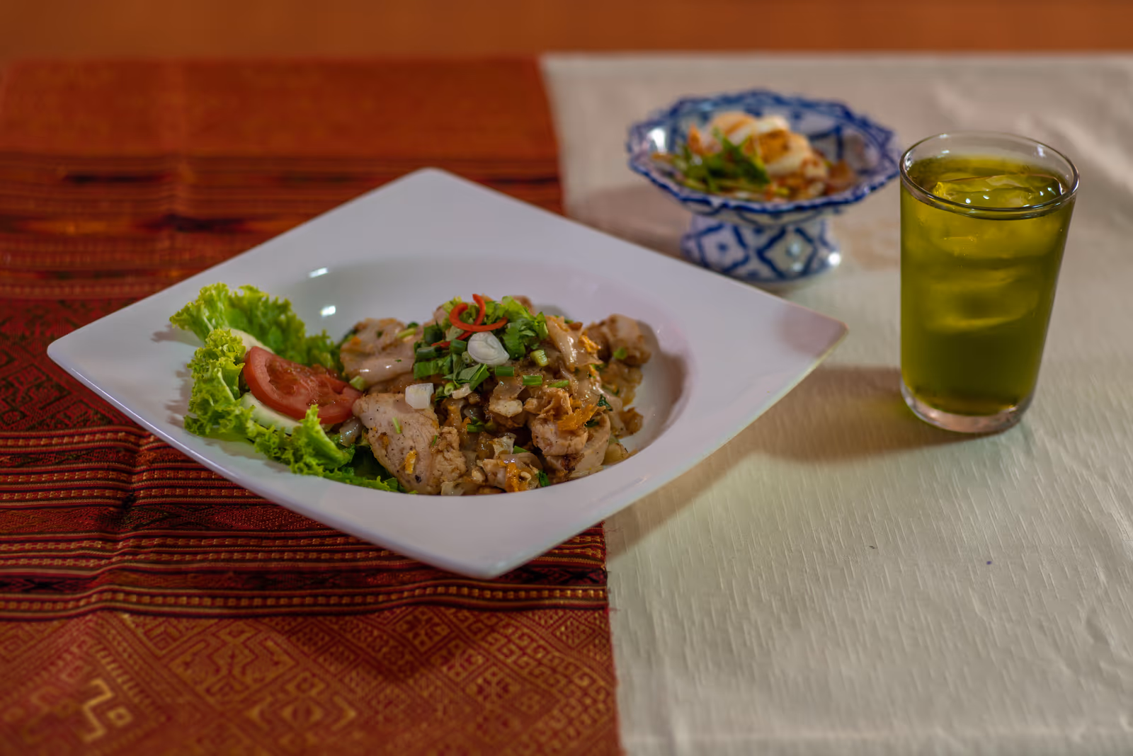A plate of fried rice and salad with a cold green drink, on a woven mat